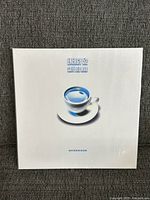 Front cover of sealed album showing blue coffee cup graphic on white sleeve