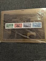 Clear photo of sealed stamp set for year 1944 with four distinct WWII themed stamps mounted on card with an artistic WW2 scene in background.