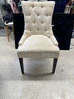 Front view of the white accent chair showing button-tufted back, white upholstery, and dark wood legs.