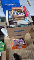 Four boxes filled with multiple James Patterson books, visible titles 'You've Been Warned' and 'Black Friday' on top in the first box.