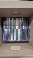 Photo showing a box filled with multiple CDs neatly stacked in two rows.