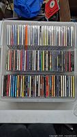 Top-down view of a plastic container filled with three rows of assorted CD jewel cases.