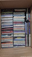 Top down photo showing a large box filled with stacked CD jewel cases. Various titles visible including EuroMix 12 and several artist albums.