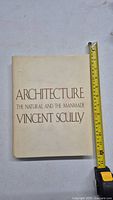 Photo of book front cover showing title 'Architecture The Natural and The Manmade' by Vincent Scully with measuring tape for size reference.