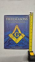 Front cover of The Freemasons book showing Masonic square and compass symbol and title