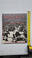 Front cover of the hockey photography book with a measuring tape showing approximately 11 inches in height, displaying the title and a historic hockey photo.