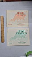 Two vintage 1974 Home Designs catalogs by Homeograph placed flat side by side with a ruler for size reference
