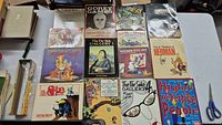 Photo showing full lot of vintage cartoon and comic books laid out on a table including Bloom County, Far Side, Gorey Games, Calvin and Hobbes and more.