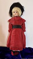 Full view of doll in red dress and black hat showing front stance