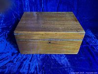 Closed rectangular antique wooden sewing box with a brass hinged lid and visible keyhole on the front. The wood has a fine grain, indicative of walnut. Slight surface wear and patina visible.