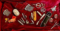 Overall assortment of silver mesh purses, brooches, scissors, cases and tools laid out on red velvet