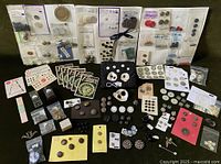 Wide image showing a diverse assortment of vintage buttons, including those attached to display cards and small bags across a dark fabric background.