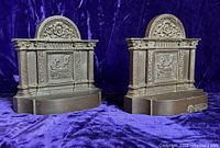 Pair of cast iron bookends side by side on purple velvet background showing front view with woman spinning relief and classical column framing.