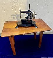 Side view of the sewing machine on the small folding table showing both items together on a dark blue surface against a light wall.