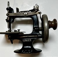 Front side view showing Singer branding, hand crank with wooden knob, cast metal body and base.
