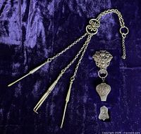 Photo showing the entire chatelaine with three silver chains and terminus tools (toothpick, tweezers, earwax spoon) laid flat on fabric.