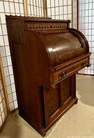 Side angle view showing burled veneer wood, roll top curve, base cupboard doors, and decorative molding on upper back edge.