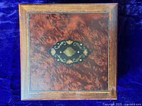 Full view of square burlwood sewing box with inlaid medallion on lid and burlwood veneer sides, showing brass keyhole on front.