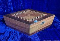 Full view of the closed wooden sewing box showing the diamond shape, lid inlay pattern, brass clasp, and wood grain.