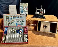 Wide shot showing entire lot: Marble Mosaics box with pieces on display, two vintage books standing behind, wooden handheld toy game, and German toy sewing machine.