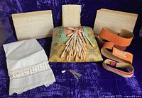Full lot showing antique lace pillow with wooden bobbins, pattern belts, lace strips, sterling bodkins, and linen apron on a purple background.