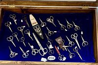 Overhead view of the scissors inside the open wooden display vitrine showing the varying sizes, handle designs, and blue velvet background.