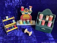 Photo showing the three thread holders together on purple velvet background with various colored spools on them.