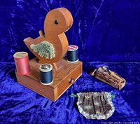 Front view of wooden Shaker bird thread holder with fabric wings and spools of thread on base, plus fabric pocket and suede sewing kit visible.