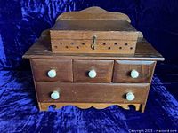 Front view of the wooden Shaker sewing box showing three small drawers above one large drawer, each with white bovine knobs; hinged box on top with brass eyelets and latch.