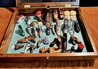 Open wooden vitrine lined in green felt showing array of miniature shoes and accessories.