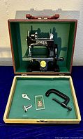 Singer child's sewing machine model SewHandy 20 inside green-lined two-tone stitched hard carry case, showing machine and accessories including clamp, gauge, and needles.