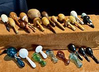 Top-down overview of 13 wooden sock darners on riser and 9 hand-blown glass sock darners on cloth background
