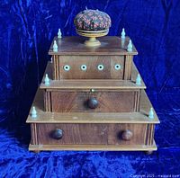 Front view showing three tiers of the box, wooden drawer knobs, inlaid trim, and white eyelet finials.