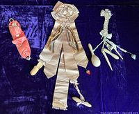 All three ribbon chatelaines shown laid out on a dark purple velvet background, including pink satin ribbon with porcelain doll pincushion, gray satin ribbon with sewing tools and safety pin, and pale blue silk satin ribbon with small sewing tools.