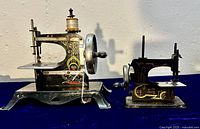 Two child’s sewing machines placed side by side on blue cloth backdrop, showing size difference and general decoration