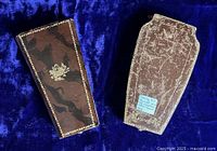 Both closed leather cases of the sewing etuis shown on blue fabric background; one case scuffed, both with gold floral stamped decoration