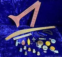 Full view of all vintage sewing advertising items arranged on dark blue velvet background showing measuring devices, tape measures, thimbles, and small sewing kits.