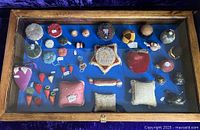 Pine vitrine with multiple pin cushions and emery bags on blue fabric