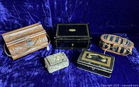 Overview of five vintage sewing kits, varying designs including wooden, metal, leather, and shell boxes set on a blue fabric.