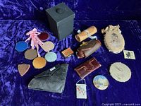 Overview of entire collection showing multiple hand-painted pinkeepers of various shapes and three different sewing kits, displayed on a purple velvet background