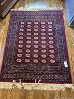 Full top-down view of red area rug with medallion pattern and fringe on hardwood floor.