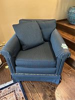 Front view of a blue and black pinstripe armchair with loose back and seat cushions and nailhead trim on the front armrests.