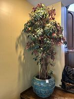 Full view of artificial tree in blue ceramic planter against a yellow wall