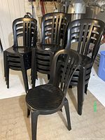 Overall view of 14 black resin stackable chairs arranged in stacks with one chair in front for a clear view of design and condition.