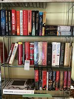Books on metal shelves with titles visible including Patterson, Follett, Silva, and others