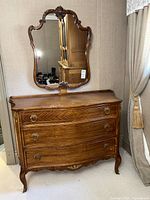 Front view of cherry wood dresser with four drawers, ring pull handles, and curved Queen Anne design. Ornate carved mirror attached above.