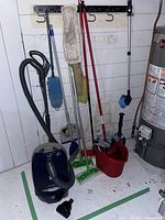 Kenmore canister vacuum, Swiffer mop and bucket, and various cleaning brushes arranged in a corner showing lot content.
