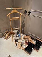 Wooden butler with tray, assorted wooden hangers, shoe shine products, brushes and wooden boxes arranged on floor against wall.