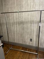 Front view of the complete assembled chrome metal clothing rack against a wall.