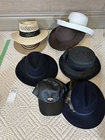Seven different hats displayed on floor including men and women styles, straw, felt and leather baseball cap.